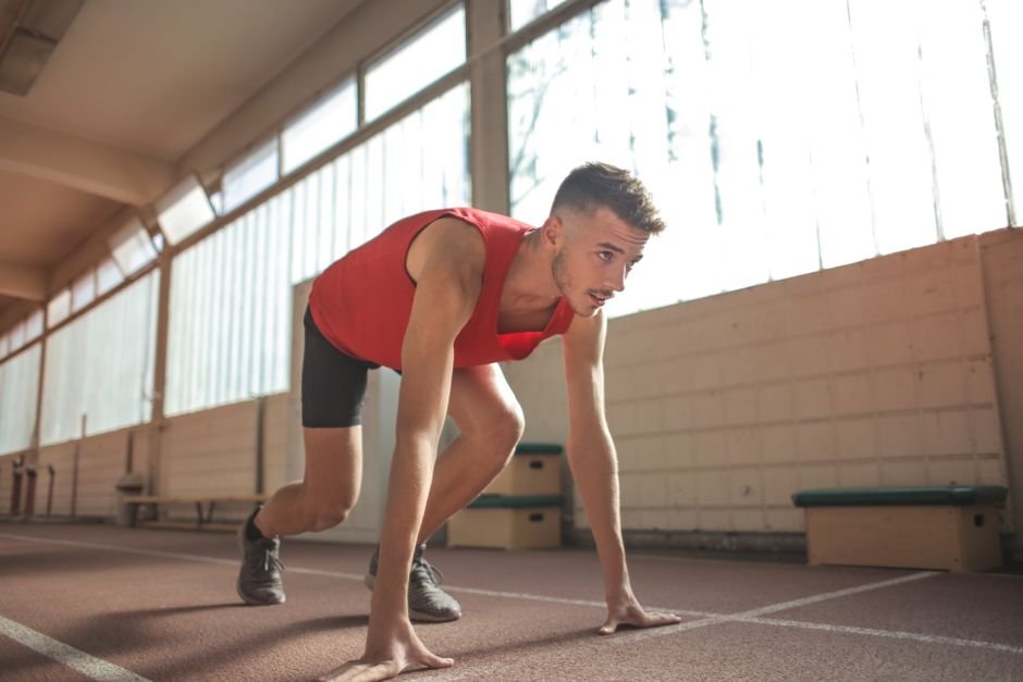 Focused male athlete in starting position indoors, ready to sprint.